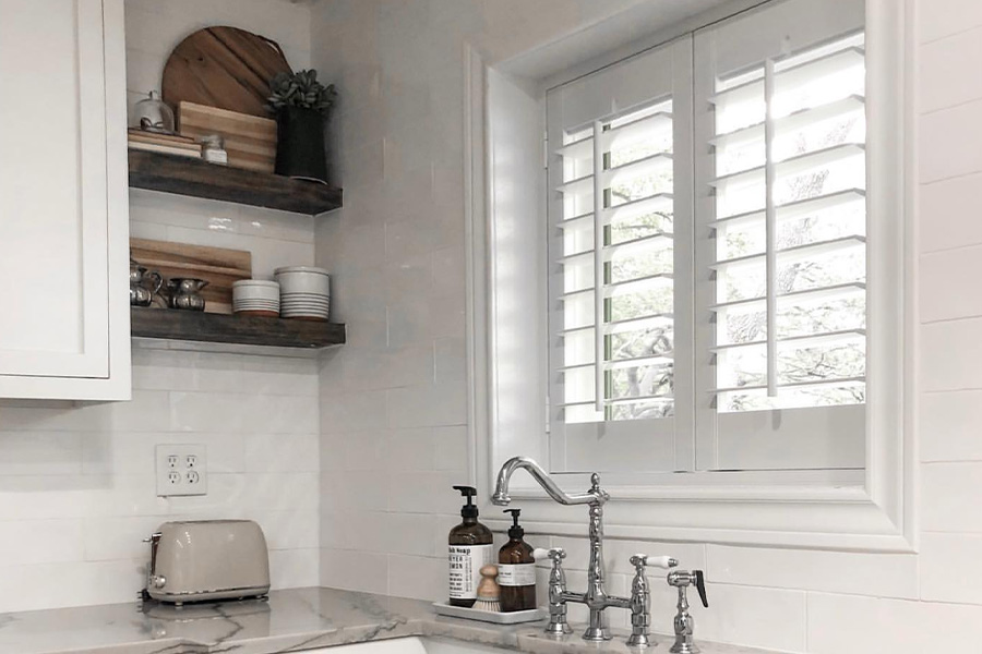 Moisture-resistant Polywood shutters are the best window treatments for a kitchen. Photo Credit: Sincerely McCraw White and sleek kitchen with Polywood shutters above a kitchen sink.